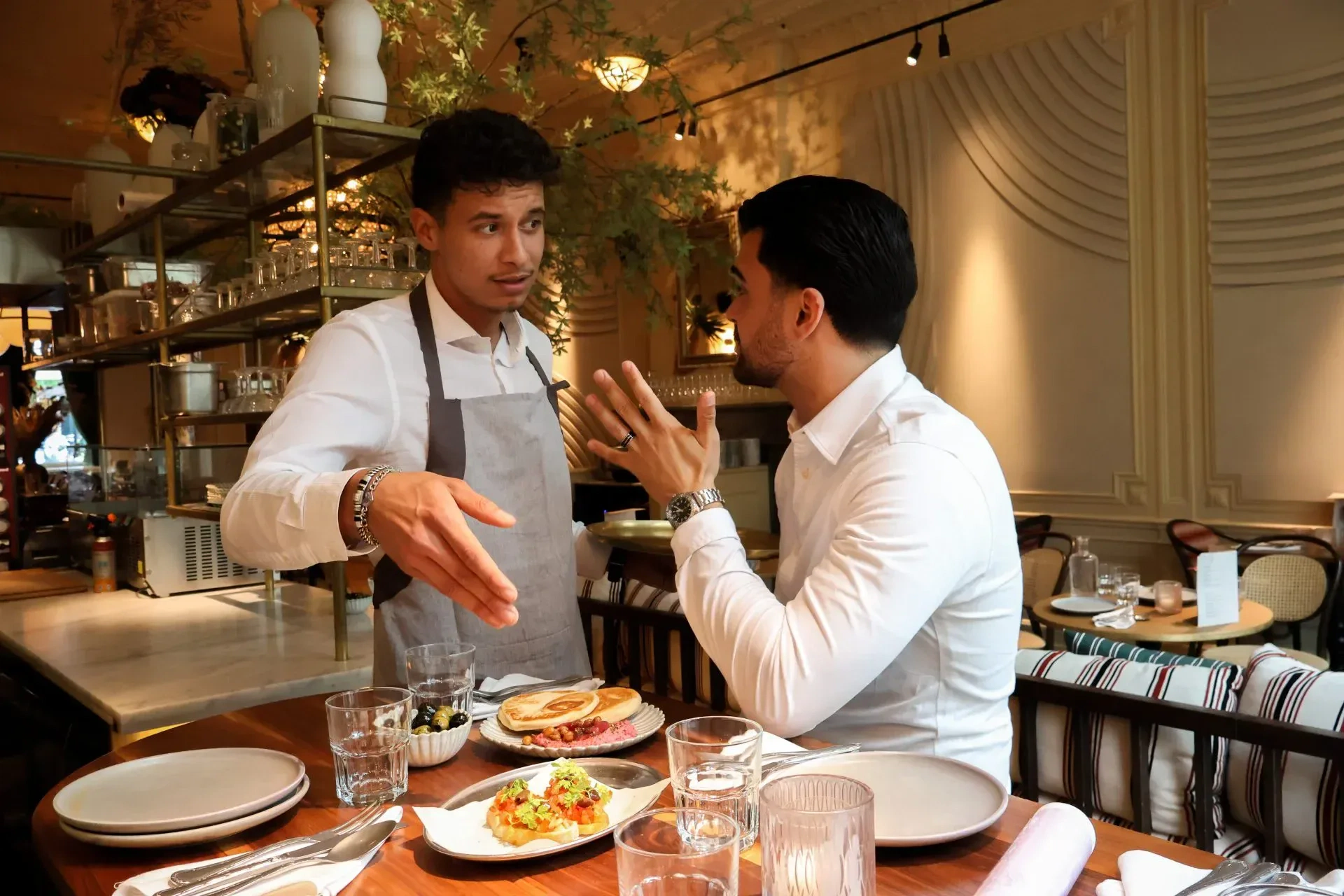 Een professionele horecamedewerker blijft kalm en glimlacht vriendelijk naar een ontevreden gast aan tafel in een restaurant.